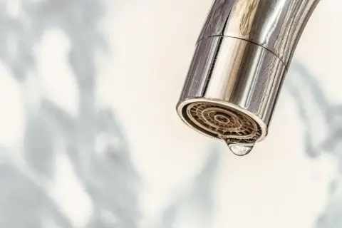 Nahaufnahme eines Chromwasserhahns mit einem Tropfen, der aus dem Sieb fällt. Zeit für das Wasserhahn Sieb reinigen.