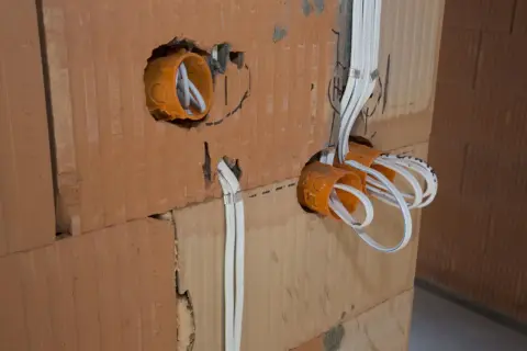 Pomarańczowe puszki elektryczne z przewodami w ścianie z cegły.