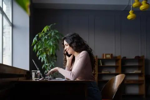 Kobieta rozmawia przez telefon, pracując przy laptopie. Dowiaduje się, jak dodać PKD do działalności, by rozszerzyć ofertę.