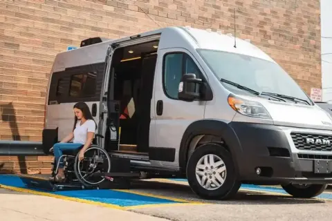 Mujer en silla de ruedas desciende de un minibus vivienda con rampa accesible.