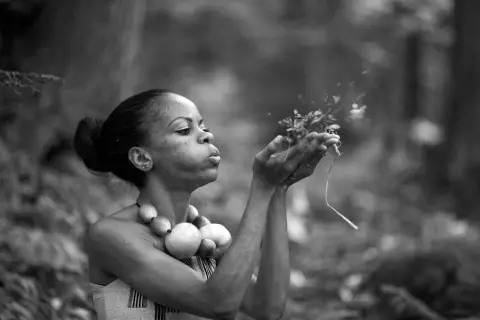 Une femme souffle sur des herbes dans cette technologie image noir et blanc. Elle porte un collier de perles rondes.