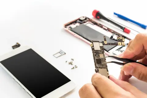 Naprawa telefonu: dłonie trzymające płytę główną, obok rozebrany smartfon i narzędzia.