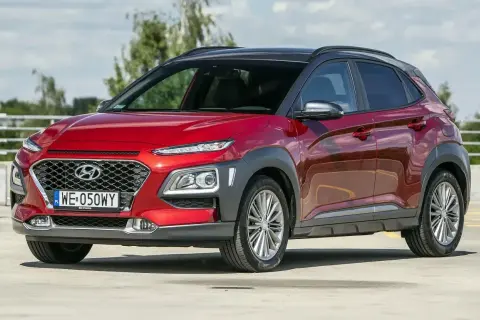 Czerwony, mały SUV dla kobiety, Hyundai Kona, z czarnym dachem, zaparkowany na zewnątrz.