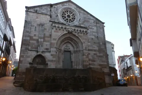 La iglesia de Santiago a Coruña, con su fachada de piedra y rosetón, se alza imponente en una calle adoquinada.