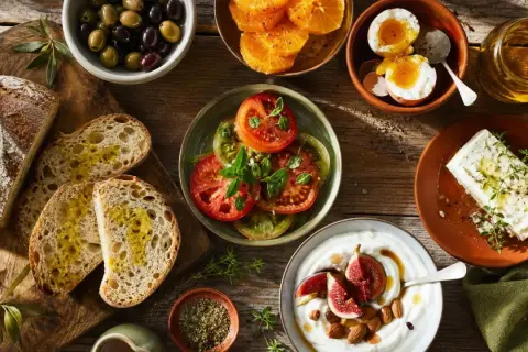 Un petit-déjeuner méditerranéen avec pain, olives, tomates, œufs, fromage, yaourt et fruits. Parfait pour savoir que cuisiner cette semaine.