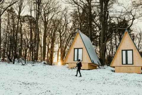 Deux tiny houses à l'année dans un paysage enneigé, entourées d'arbres. Une personne marche dans la neige.
