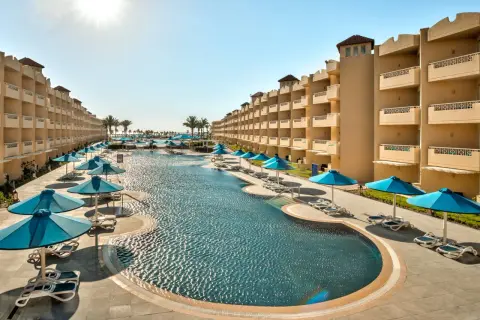 Egipt last minute all inclusive najtaniej: luksusowy basen z leżakami i parasolami, otoczony hotelowymi budynkami. Idealne miejsce na relaks.