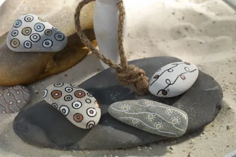 Ideas para pintar piedras de playa: piedras decoradas con círculos concéntricos y líneas onduladas en tonos tierra y blanco.