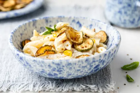 Piatto di pasta cremosa con ricotta e zucchine croccanti, guarnito con scorza di limone e menta.