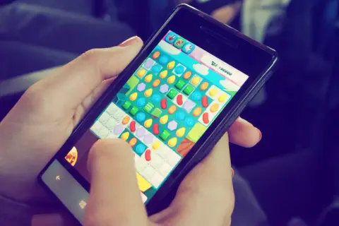 Ręce trzymają telefon, na którym widać kolorową planszę gry. To popularne gry na telefon, które umilają czas w podróży.