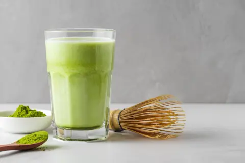 Un verre de matcha crémeux, une cuillère de poudre verte et un fouet traditionnel. Idéal pour une femme enceinte cherchant une boisson saine.
