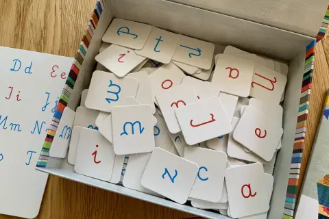 Zestaw kart z literami do nauki pisania dla dzieci. Litery w kolorze niebieskim i czerwonym, na białych kwadratach.