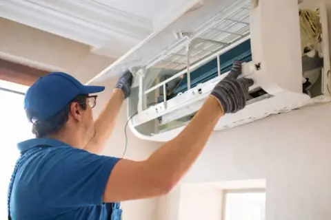 Fachowiec w niebieskiej czapce i rękawiczkach montuje klimatyzację w domu, dbając o każdy szczegół instalacji.