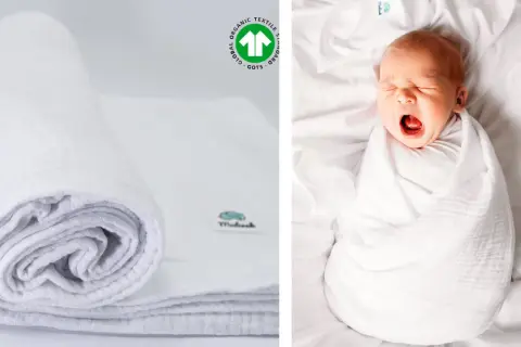 Biały, zwinięty otulacz muślinowy obok śpiącego niemowlaka. Certyfikat GOTS potwierdza jego ekologiczne pochodzenie.