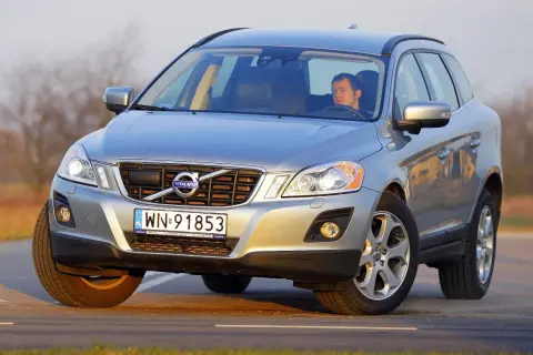 Srebrne Volvo XC60 z mężczyzną za kierownicą na drodze. Wiele osób szuka **volvo xc60 opinie** przed zakupem.