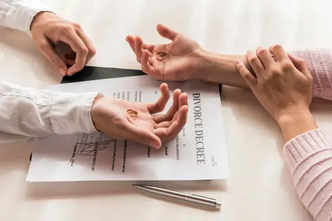 Dwie dłonie trzymają obrączki na tle dokumentu "DIVORCE DECREE". Pozew o rozwód z orzekaniem o winie.