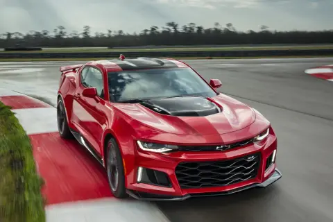 Czerwone Camaro ZL1 z czarnymi pasami na masce i dachu pędzi po torze wyścigowym, zostawiając za sobą smugę.