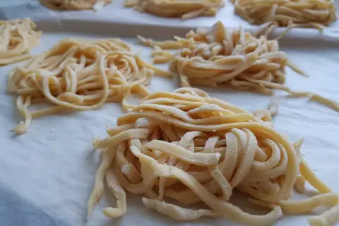 Domowy przepis na makaron do rosołu. Świeże, żółte nitki makaronu ułożone na papierze do pieczenia, gotowe do suszenia.