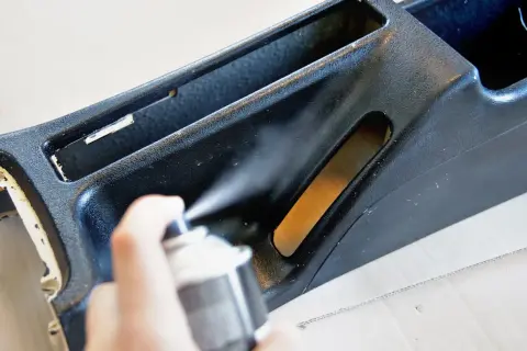 Ręka trzyma puszkę z farbą w sprayu, odświeżając czarne plastiki w aucie.