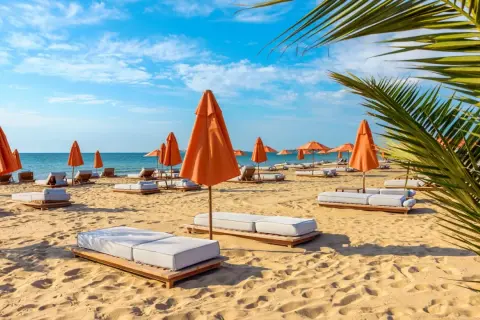 Słoneczny dzień na plaży z pomarańczowymi parasolami i leżakami na złotych piaskach.