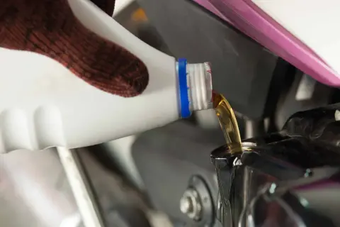Rękawica wylewa olej do silnika motocykla. Pamiętaj, co ile wymieniać olej w motocyklu, by służył Ci długo.