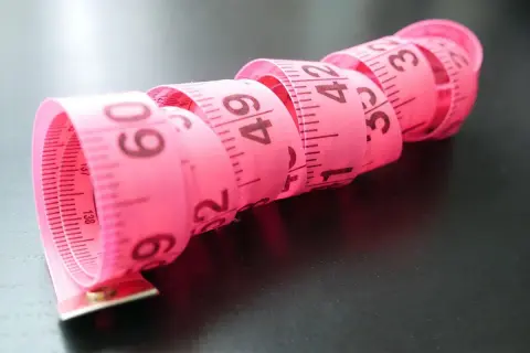 Różowa miarka krawiecka zwinięta w spirale, z widocznymi centymetrami. Idealna do określenia rozmiaru buta 2 latka.