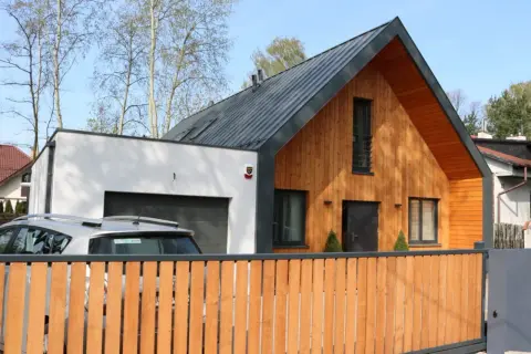 Nowoczesny dom z drewnianą dobudówką do części murowanej, z garażem i drewnianym płotem.