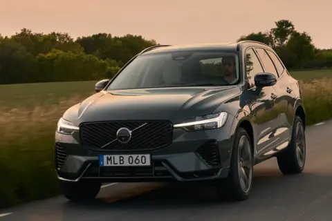 Ciemnoszary Volvo XC60 2025 jedzie drogą wśród zieleni o zachodzie słońca.