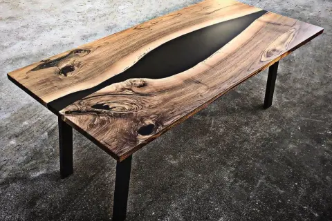 Tavolo in legno con venature naturali e un inserto centrale di resina per tavoli nera, che crea un contrasto moderno e affascinante.