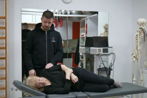 Fizjoterapeuta bada pacjentkę leżącą na kozetce.