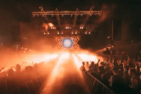 Foule en délire sous les lumières oranges d'une scène, un visuel psychédélique au centre. Photographie événementielle capturant l'énergie d'un concert.