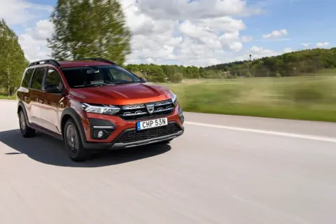 En röd Dacia Jogger begagnad kör på en landsväg i Sverige. Bilen är i rörelse med suddig bakgrund.
