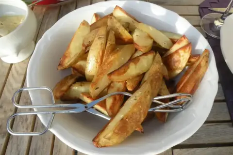 En skål med gyllene klyftpotatis i ugn, redo att serveras med tång.