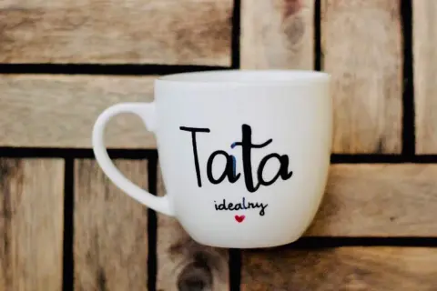 Biały kubek z napisem "Tata idealny" i serduszkiem. Świetny pomysł, jak zrobić prezent dla taty.