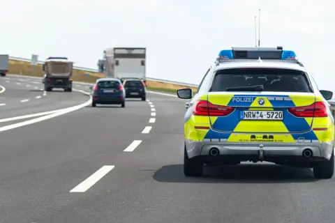 Niemieckie autostrady: radiowóz policyjny z włączonymi sygnałami świetlnymi jedzie za innymi pojazdami.