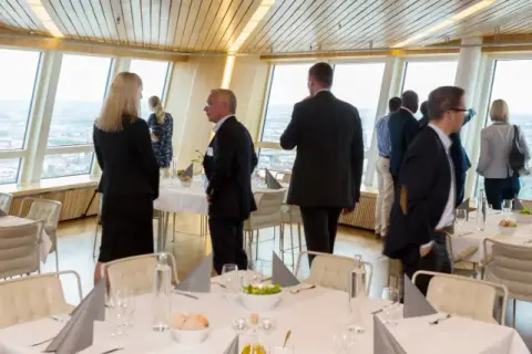 Människor i affärs kläder njuter av utsikten från en restaurang. En turning torso visning av staden.