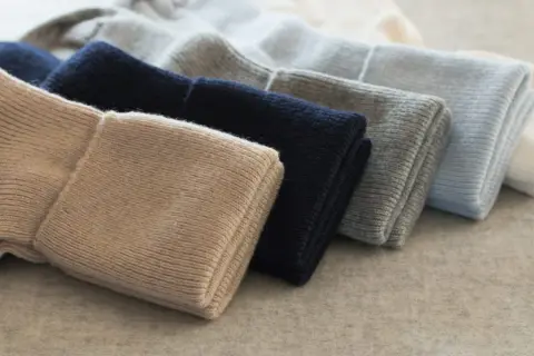 Gestapelte Mützen in Beige, Dunkelblau, Grau und Hellblau. So pflegt man Kaschmir, damit er lange schön bleibt.