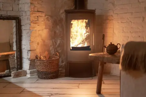 Un accogliente impianto riscaldamento a legna con fiamme vive, cesto di legna e teiera su un tavolino rustico.
