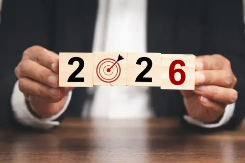 Ręce trzymają kostki z napisem "2026" i tarczą celowniczą. To symboliczne przedstawienie celów i planowania, jak środki trwałe co to, w kontekście przyszłości.
