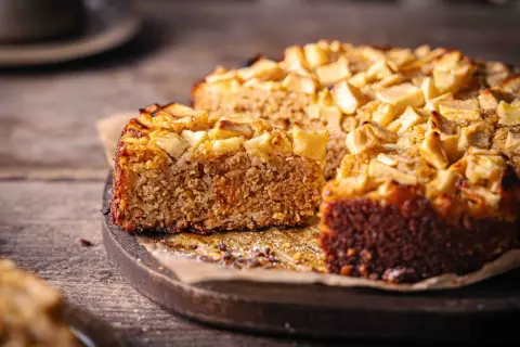 Ein saftiger Haferflocken Kuchen mit Apfelstücken, auf einem Holzbrett, bereit zum Genießen.