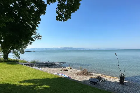 Słoneczny dzień nad Jeziorem Bodeńskim. Plaże z kamykami, łodzie i zielona trawa zapraszają do relaksu.