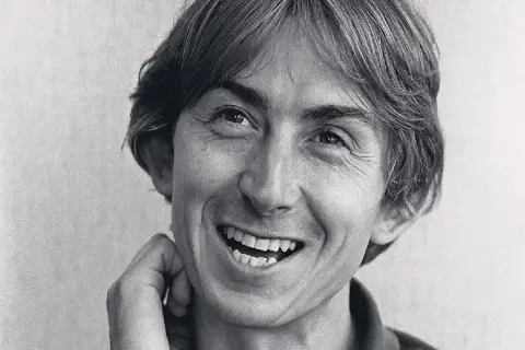 Black and white close-up portrait of Mark Hollis of Talk Talk smiling with his hand near his face.