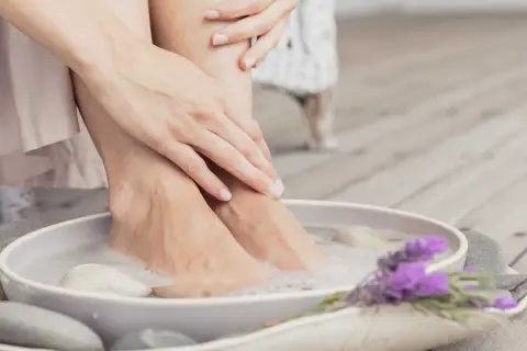 Détente avec un bain de pied maison, pieds dans l'eau savonneuse, galets et lavande.