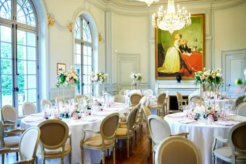 Salle de réception élégante avec tables rondes dressées pour un mariage. Un tableau ancien domine la pièce, offrant une idée de plan de table mariage.