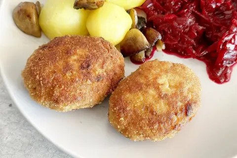Dwa złociste kotlety mielone z indyka, podane z ziemniakami, grzybami i buraczkami.