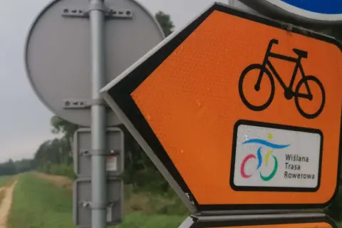 Pomarańczowy znak kierunkowy z rowerem i napisem "Wiślana Trasa Rowerowa" wskazuje drogę.