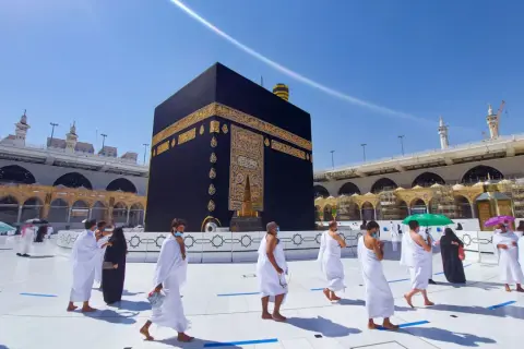 Pielgrzymi w białych strojach okrążają Kaabę, święte miasto islamu, w słoneczny dzień.