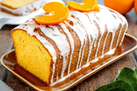 Omas saftiger Orangenkuchen, mit Zuckerguss und frischen Orangenscheiben garniert, duftet herrlich auf dem rustikalen Holztisch.