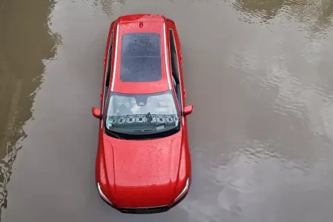 Czerwony samochód stoi w wodzie. Po powodzi czeka go osuszanie auta.