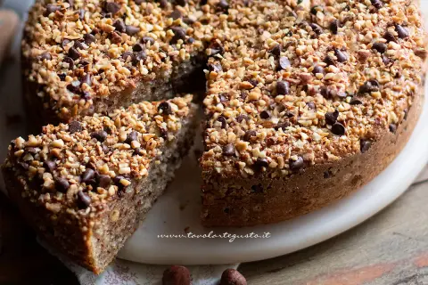 Una deliziosa torta di nocciole, ricoperta di granella croccante e gocce di cioccolato, con una fetta tagliata.